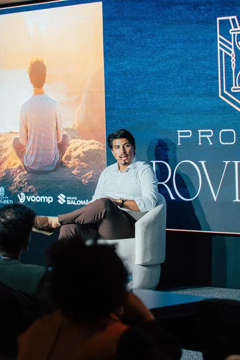 Palestrante sentado no palco diante de painel de meditação